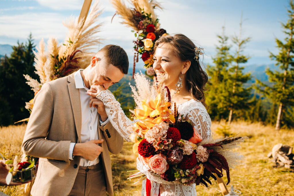 Newlyweds exchange rings during their beautiful wedding ceremony outdoors. 
The groom kisses the hand of his wife