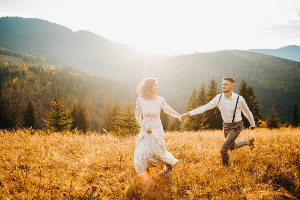 Happy gorgeous bride and stylish groom run and having fun, boho wedding couple, luxury ceremony at mountains with amazing view